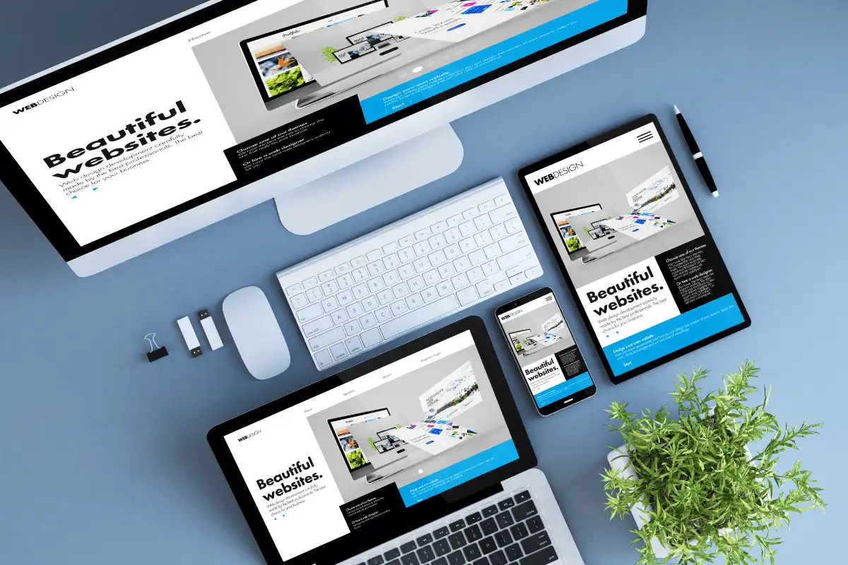 responsive website displayed on multiple devices including laptop, tablet, mobile phone and large monitor on blue background with plant, mouse and usbs