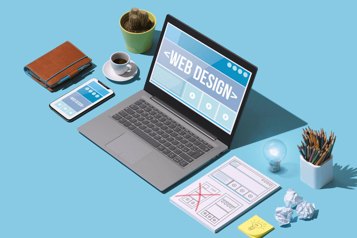 illustration of laptop with the words web design on a blue table with laptop and office supplies